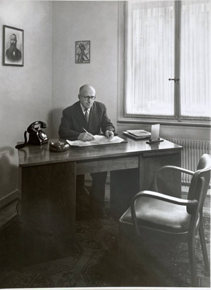 Leon Zuckermann, le grand-oncle d'Adam Lassner, dans son bureau à La Chaux-de-Fonds dans les années 1950. Au-dessus, le portrait de Baruch Reinin, qui a démarré la tradition horlogère familiale en Russie au 19ème siècle.