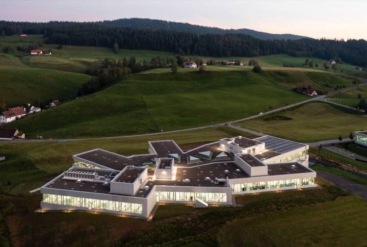 Le nouveau site des Saignoles au Locle: 10'400m2 d'ateliers répartis sur plusieurs demi-niveaux qui s'adaptent à la topographie et aux flux industriels. Le bâtiment est équipé de larges fenêtres en SageGlass, un verre électrochrome qui se teinte en fonction de la lumière. Deux chaudières à pellet et une pompe à chaleur évitent toute énergie fossile pour le chauffage. Le toit est recouvert de 300 panneaux photovoltaïques sur une surface de 480m2 pour une production énergétique de 80kW.