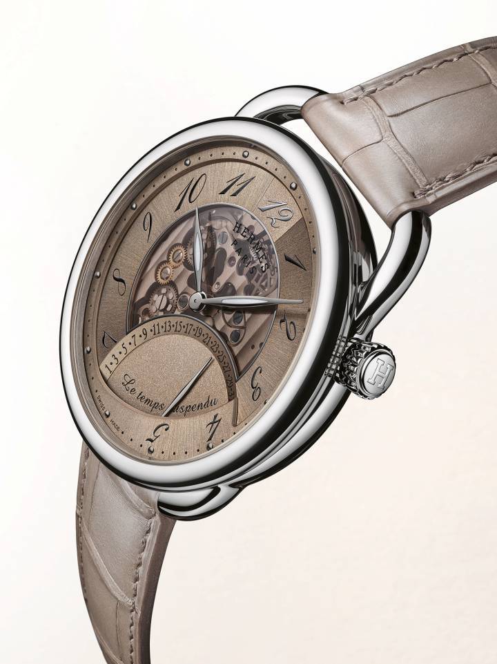 Arceau Le Temps Suspendu: réinterprétation du modèle de 2011, Arceau Le temps suspendu présente une nouvelle esthétique. Son boîtier affiné de 42 mm révèle un cadran ajouré qui laisse entrevoir le module exclusif «Le temps suspendu». Celui-ci est rythmé par le mouvement de manufacture Hermès H1837 visible à travers le fond transparent. En or gris ou rose, les boîtiers s'associent à trois coloris de cadrans — brun désert, rouge sellier et bleu —, réaffirmant l'intemporalité de la ligne aux attaches asymétriques caractéristiques, réalisés dans les ateliers d'Hermès Horloger.