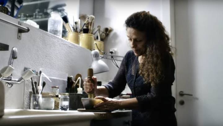 Anita Porchet prépare tous ses émaux manuellement, dans son atelier. Ici, elle broie du verre coloré à l'aide d'un pilon jusqu'à l'obtention de particules colorées aussi fines que le sable. C'est ensuite, dans une solution aqueuse qu'elle pourra les appliquer sur le cadran.