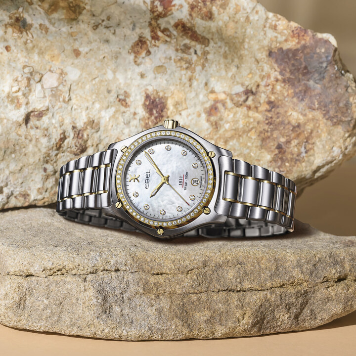 L'Ebel 1911 Grande arbore un cadran en nacre rehaussé de diamants et une lunette sertie de diamants. Or jaune 18 carats et acier inoxydable.