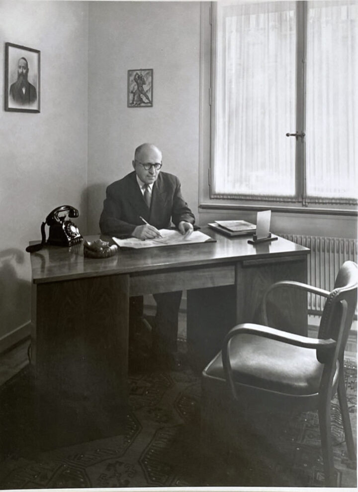 Leon Zuckermann, le grand-oncle d'Adam Lassner, dans son bureau à La Chaux-de-Fonds dans les années 1950. Au-dessus, le portrait de Baruch Reinin, qui a démarré la tradition horlogère familiale en Russie au 19ème siècle.